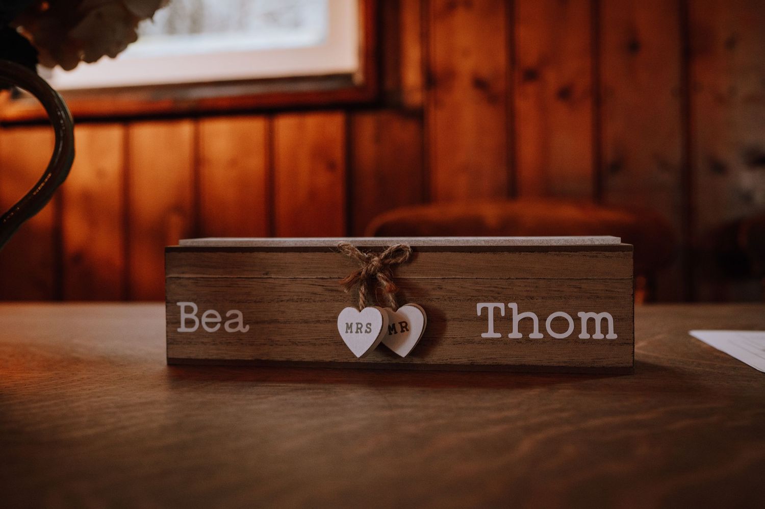 A wooden box with 'Bea Thom' engraved and two heart decorations sits on a brown surface.