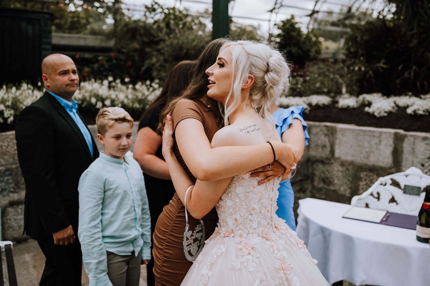 Wedding guests share emotional hugs during an outdoor reception with table settings.