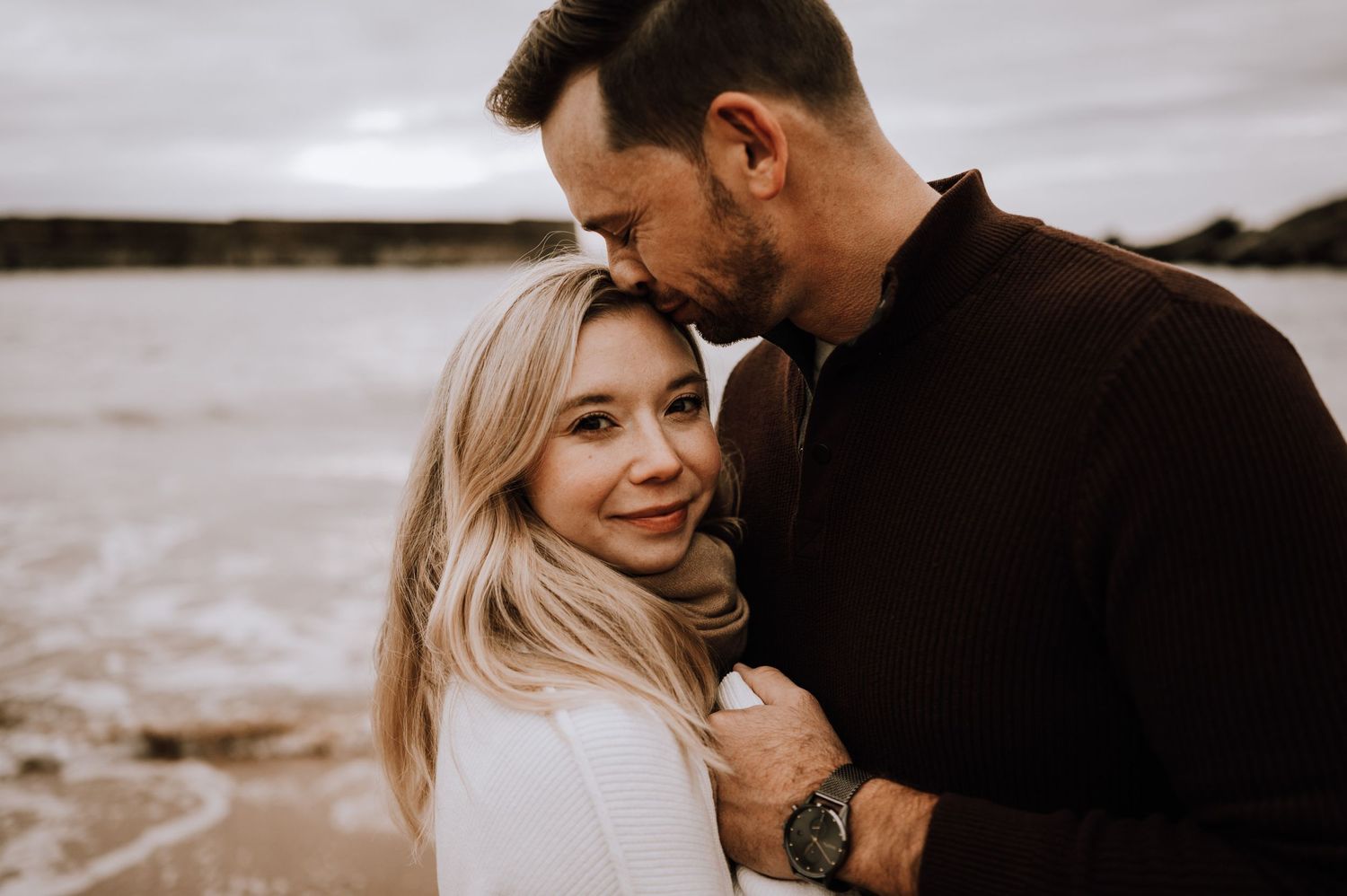 A tender moment shared between two people against a coastal backdrop.