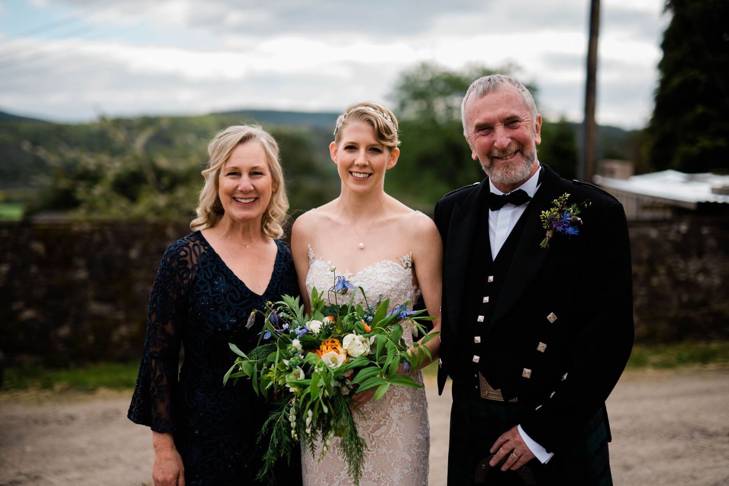 Outdoor wedding portrait against scenic hillside backdrop with floral bouquets.