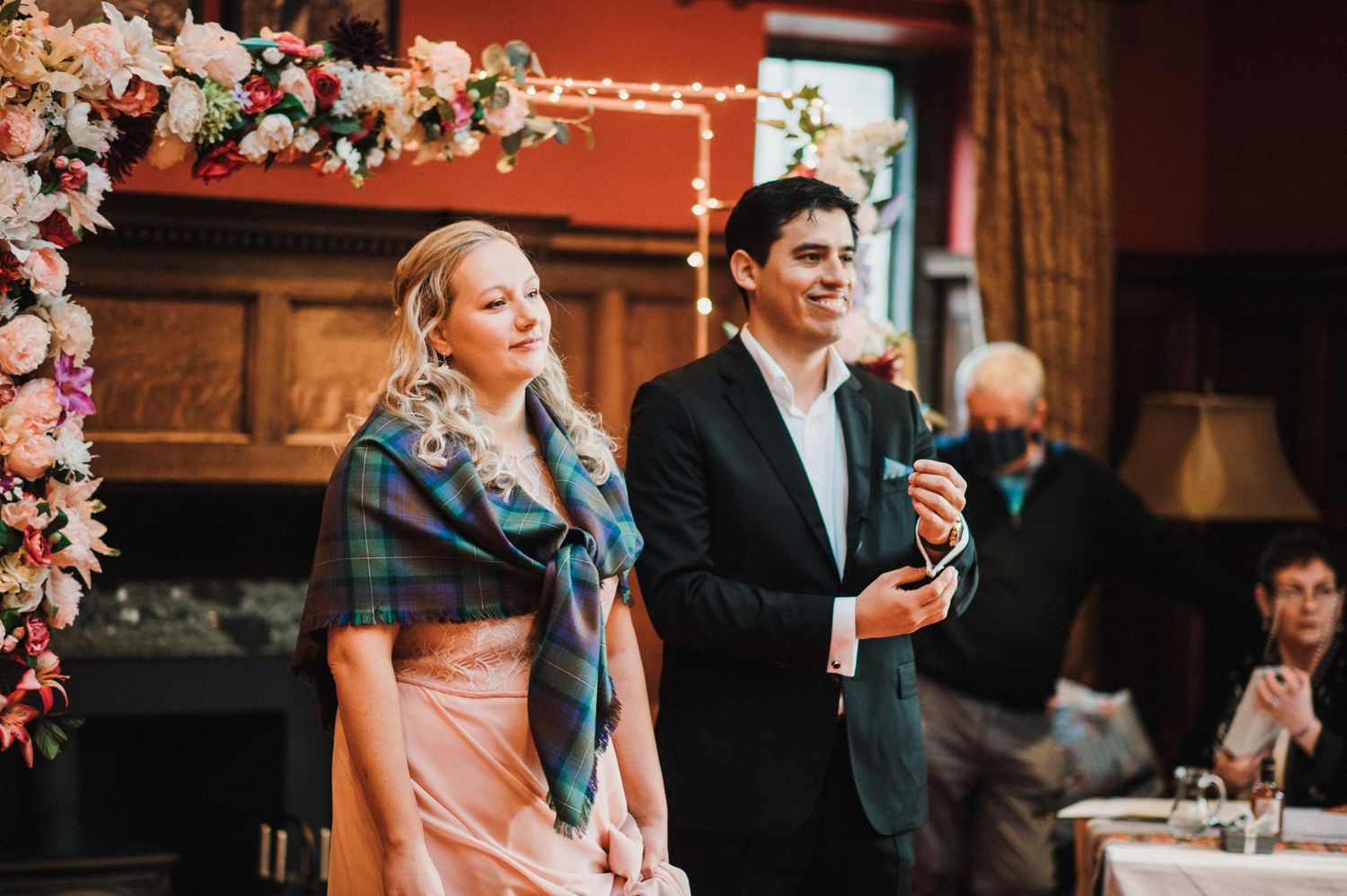 Wedding ceremony scene with floral arch and couple standing before guests.