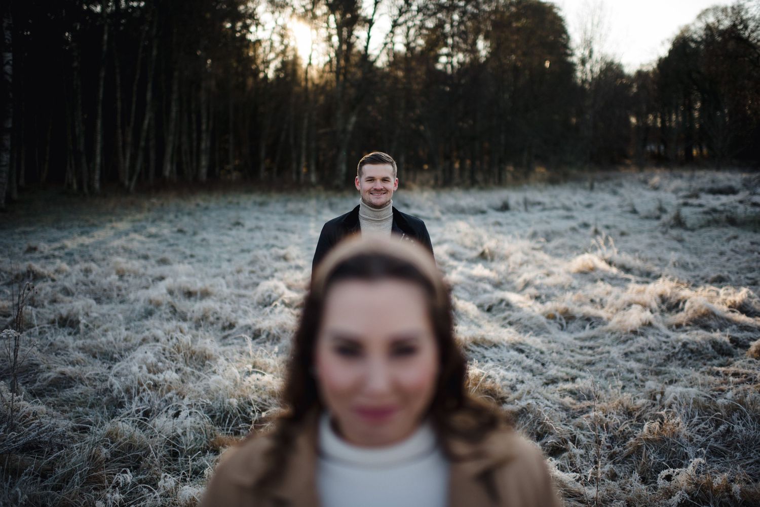 A creative engagement photo with selective focus on the couple in a frosty winter field.