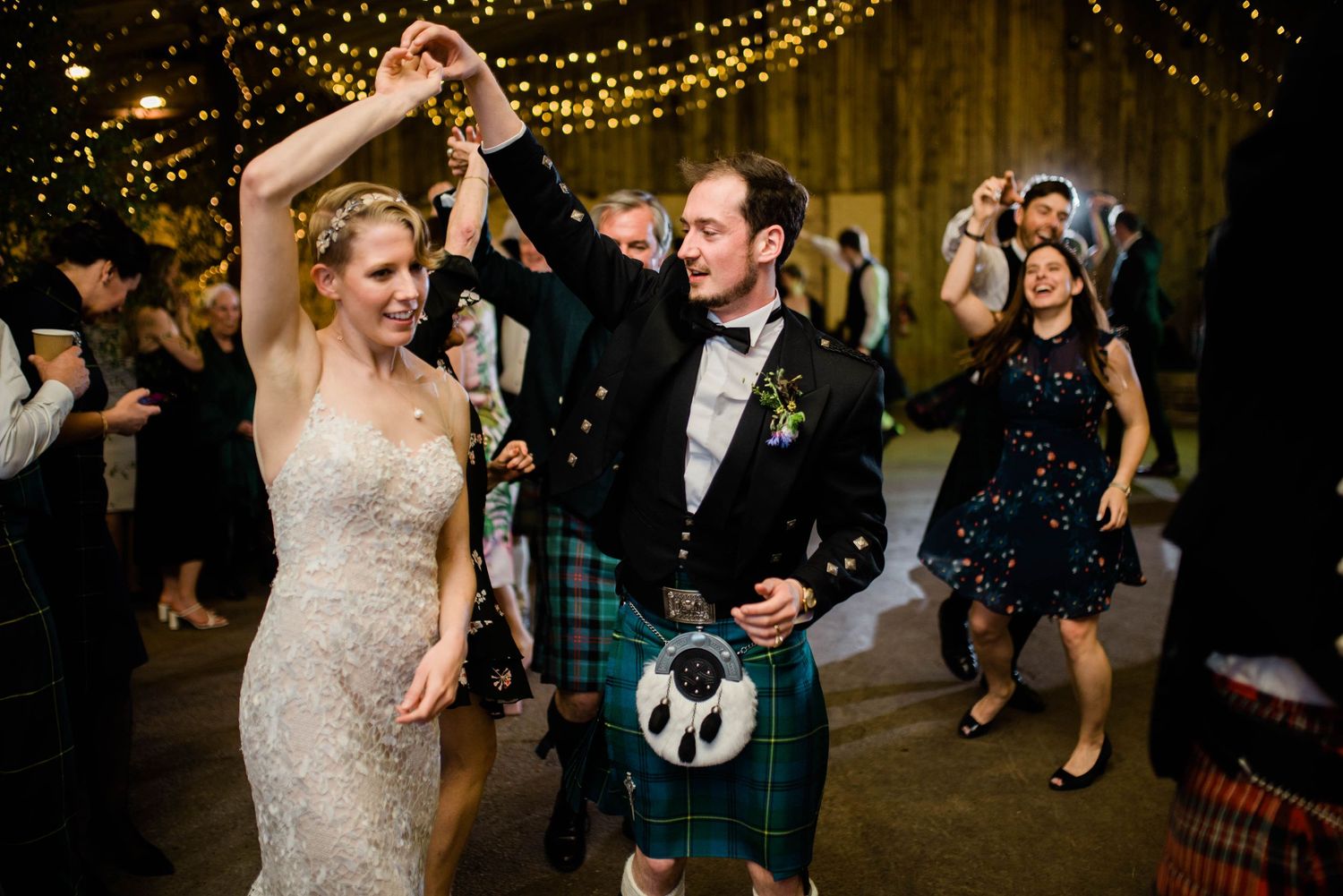 Dancing guests celebrate at a Scottish wedding reception under warm string lights.