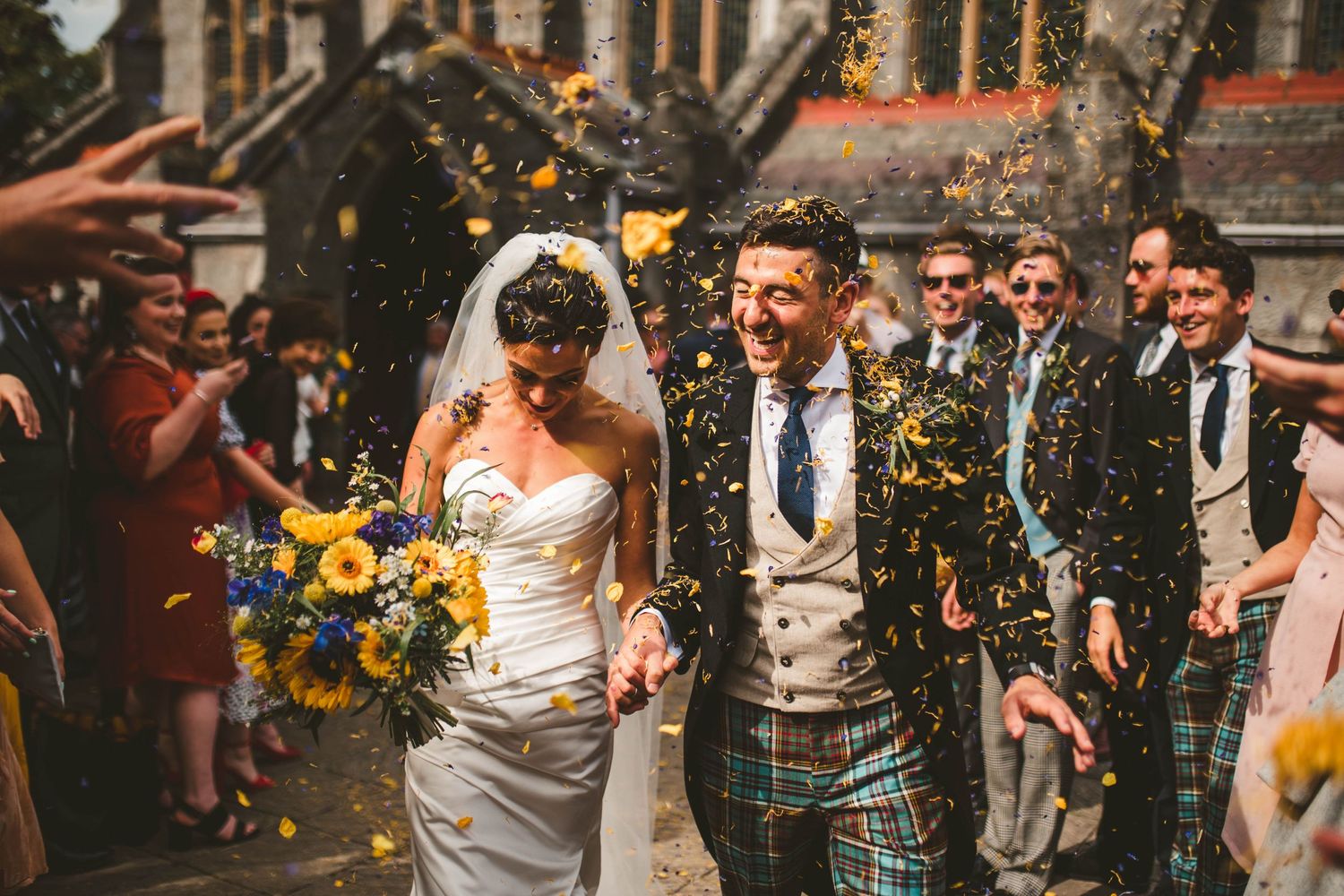 Wedding party exits church while guests throw confetti in celebration.