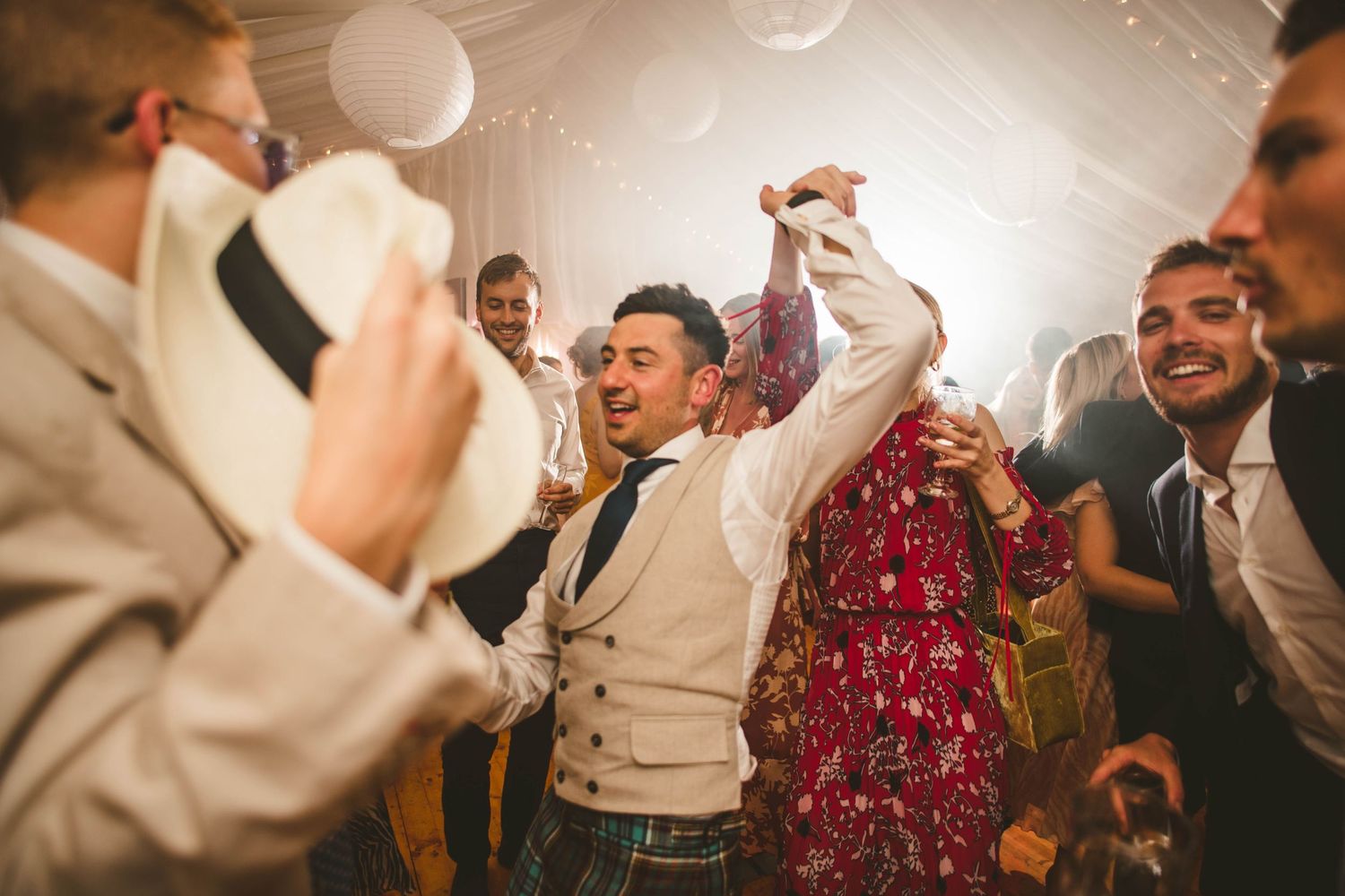 Joyful wedding guests dancing and celebrating at a reception under hanging lanterns.