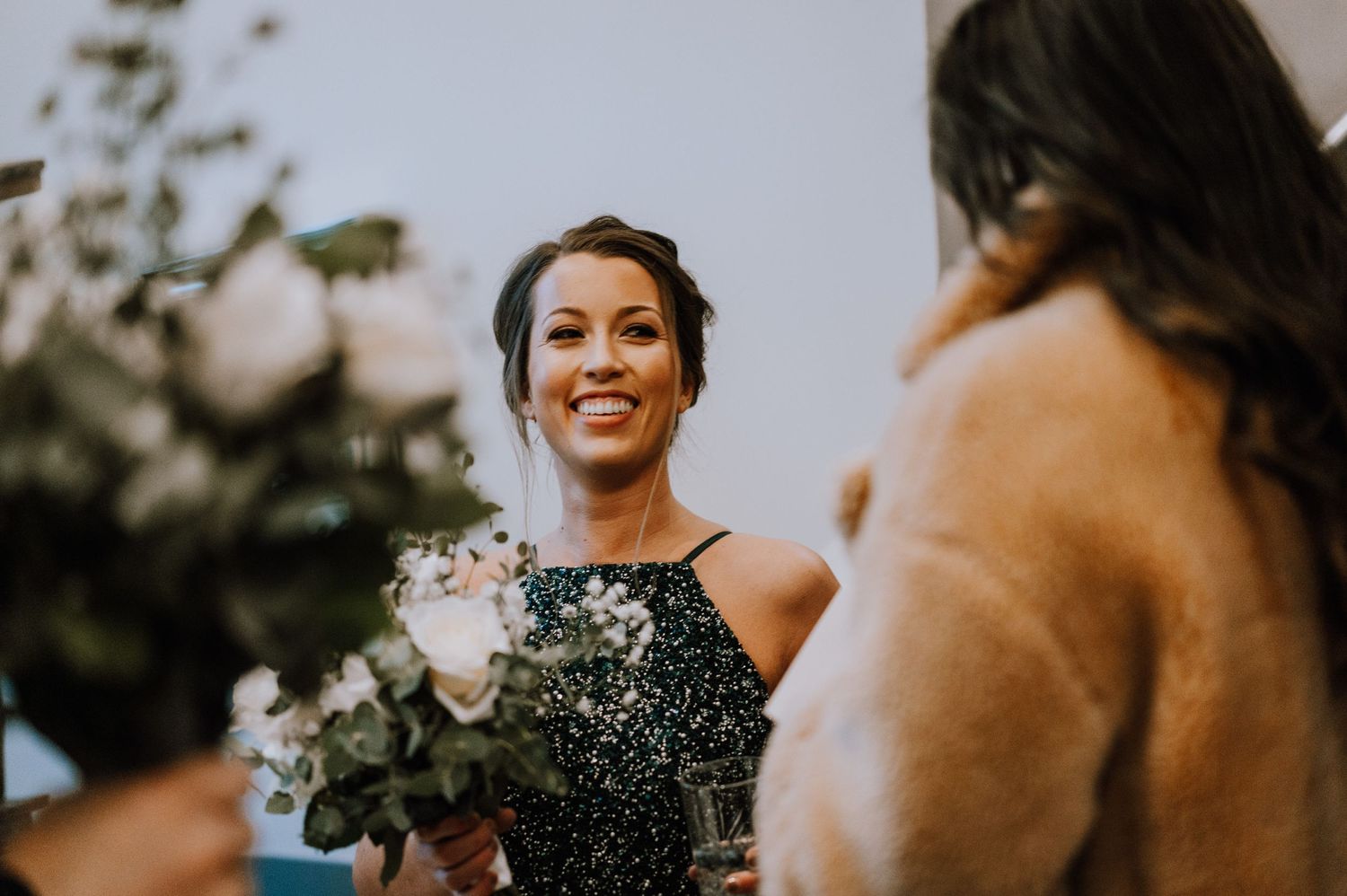 Wedding guests in sparkly dresses share a cheerful moment with bouquets.