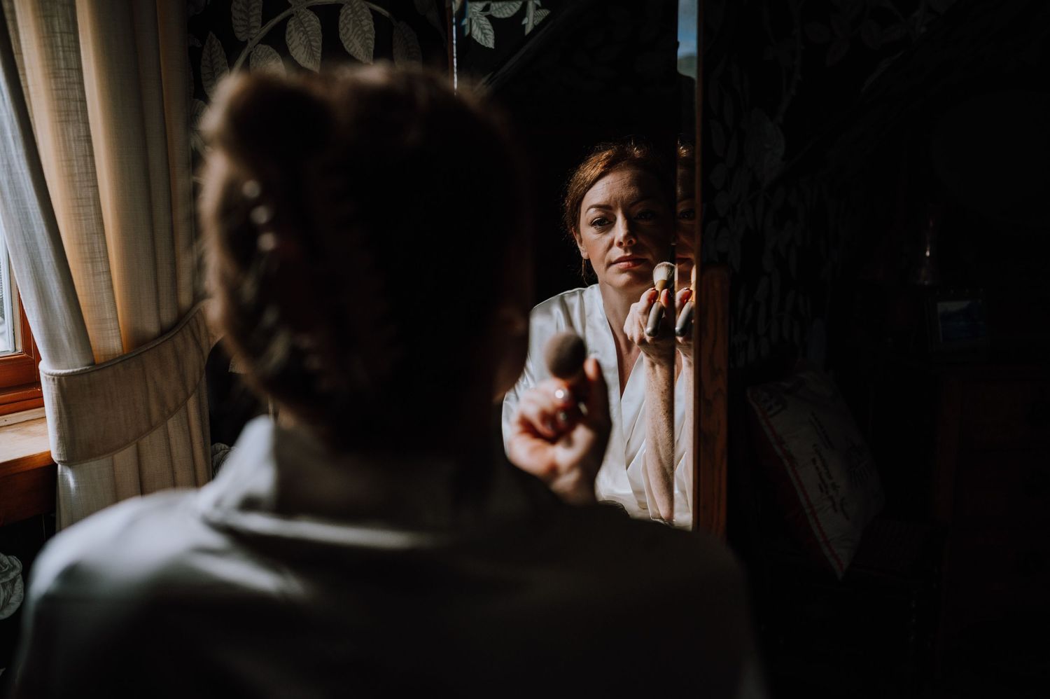 A reflection in a mirror during wedding preparations in a dimly lit room.
