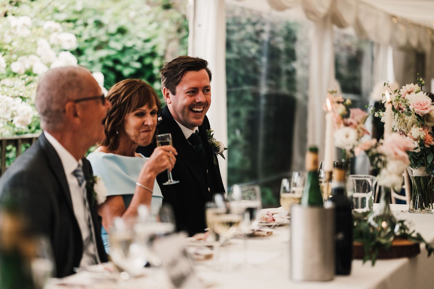 Candid moment of guests sharing toasts and laughter during wedding reception speeches.