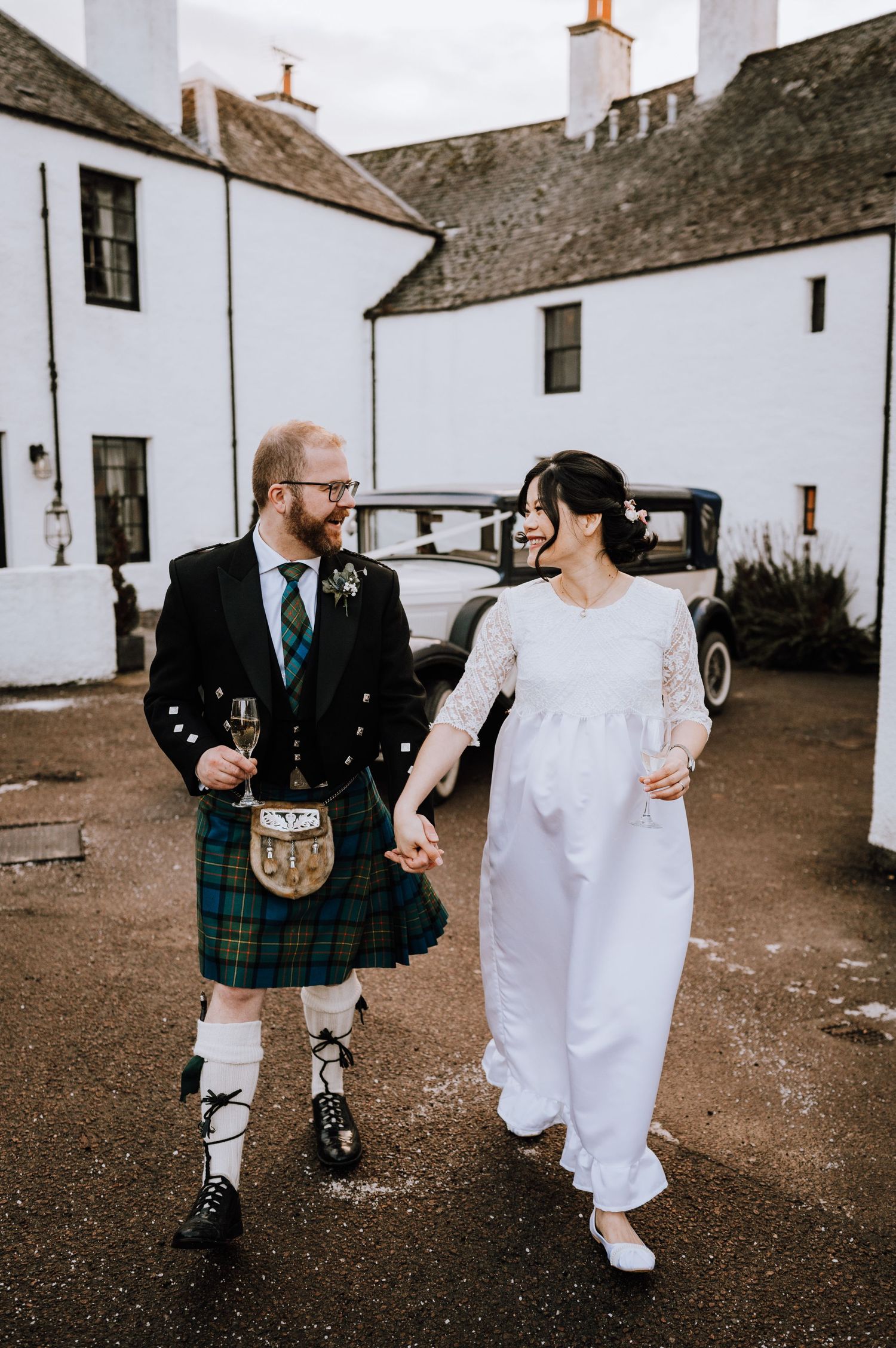 Bride and groom walking hand in hand, with the groom wearing traditional Scottish kilt attire.