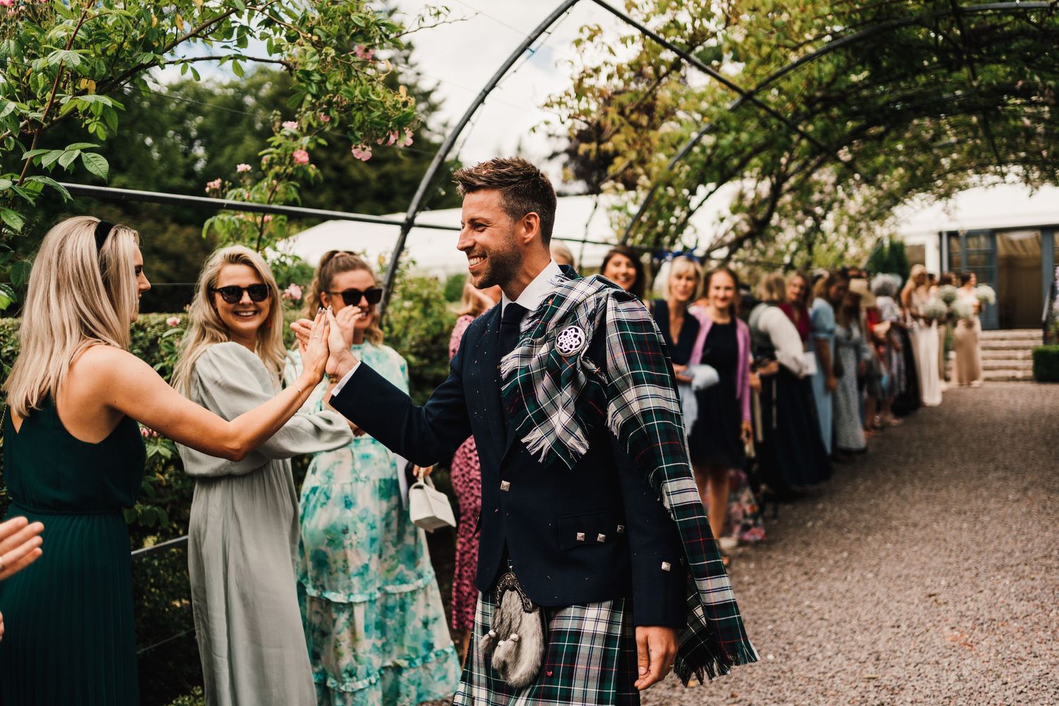 Wedding guests celebrate with high-fives along a garden pathway.