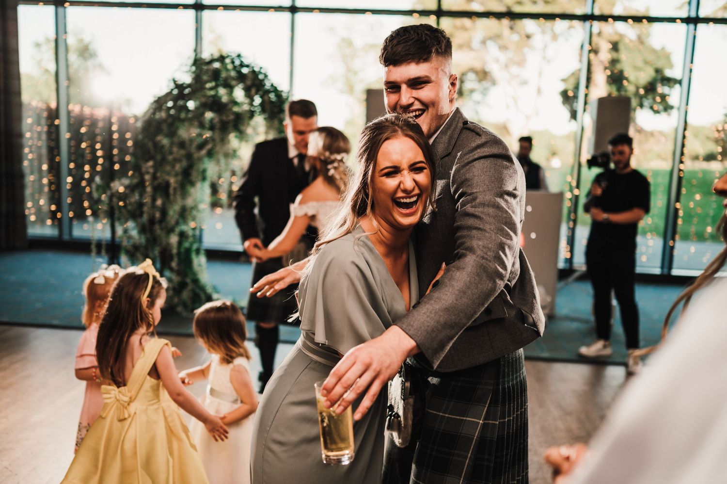 Happy dancing at a wedding reception with a little girl in yellow dress visible in background.