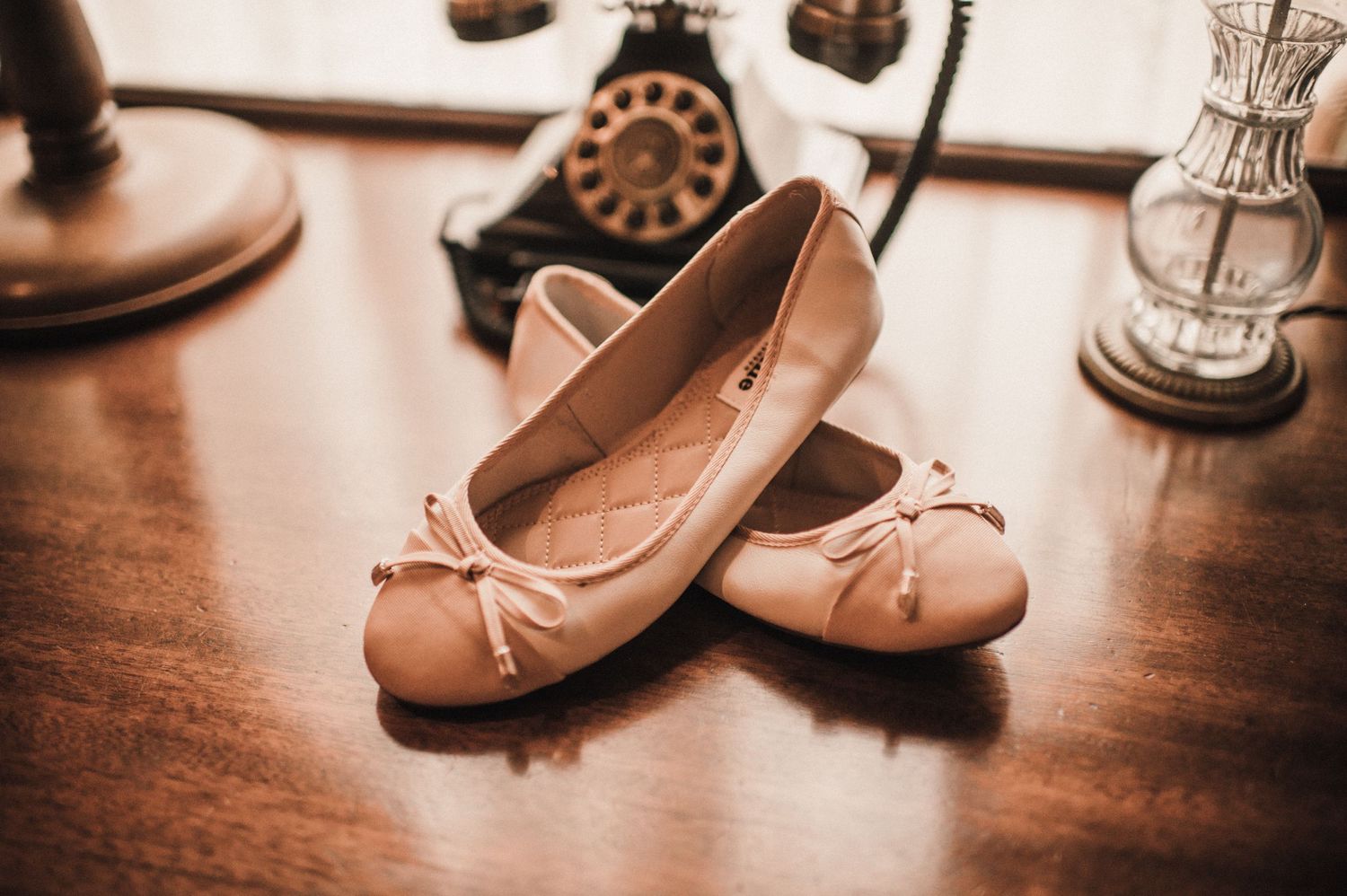 Pink ballet flats with bow details on a wooden surface next to vintage decor items.