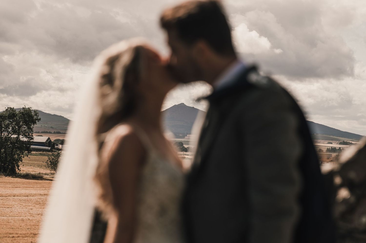 Silhouetted wedding couple against dramatic cloudy sky and mountain landscape.