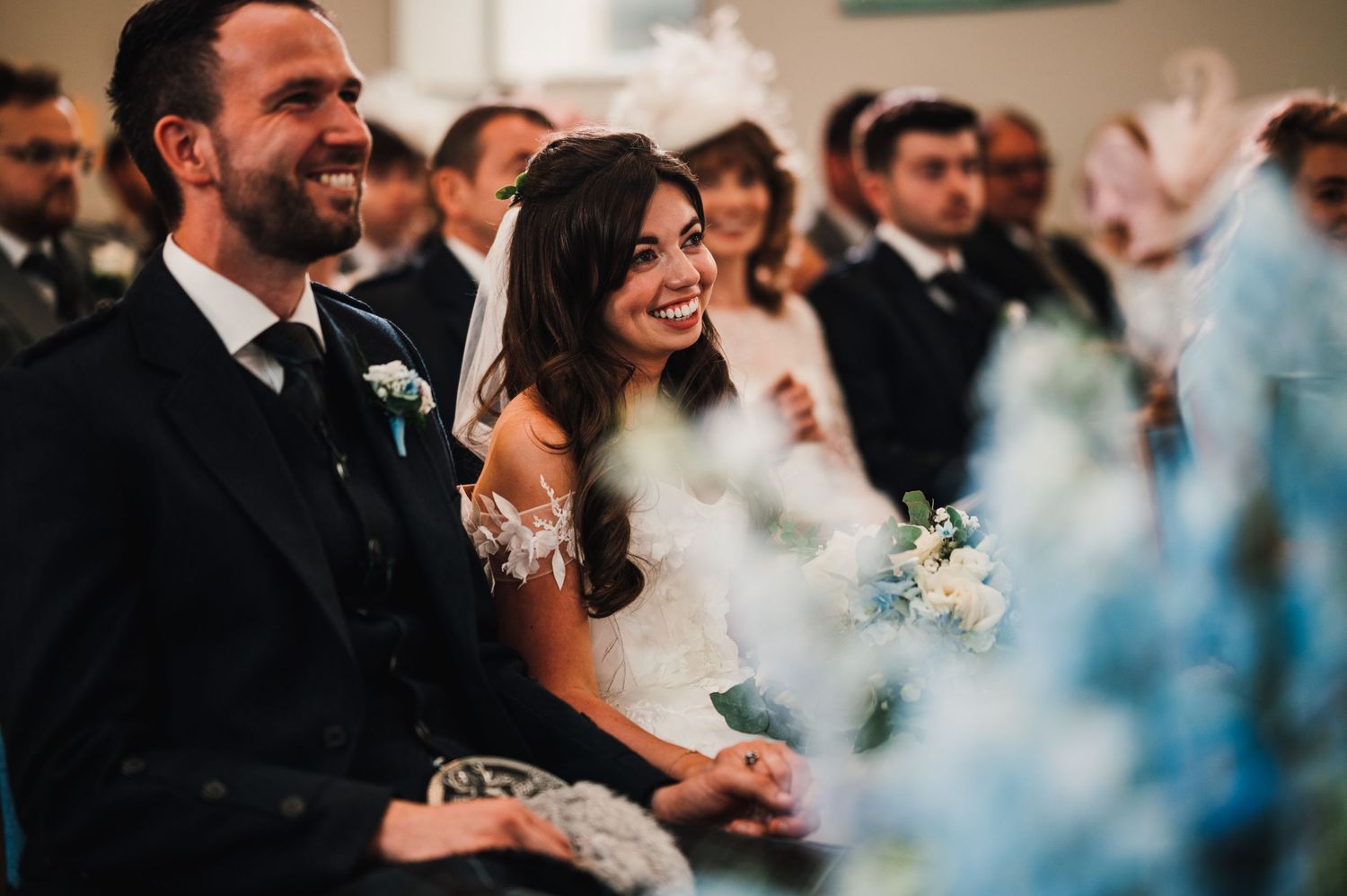 A joyful wedding ceremony moment with blue floral decorations and natural light streaming in.