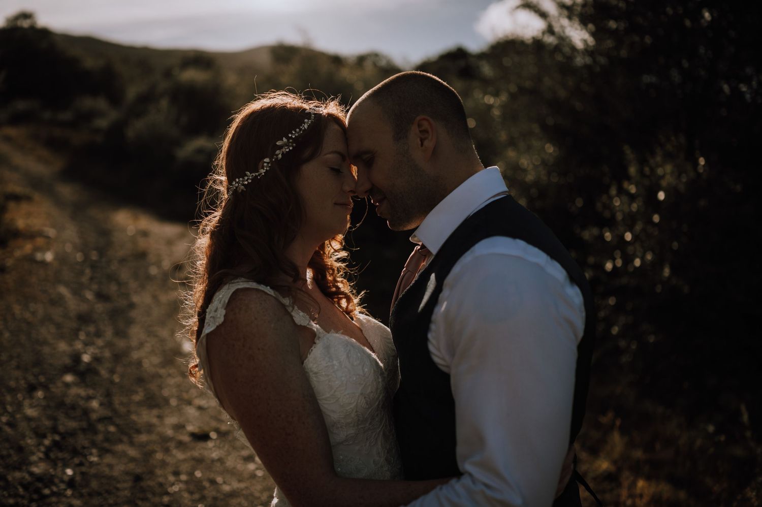 A romantic wedding moment captured in golden backlight on a mountain trail.
