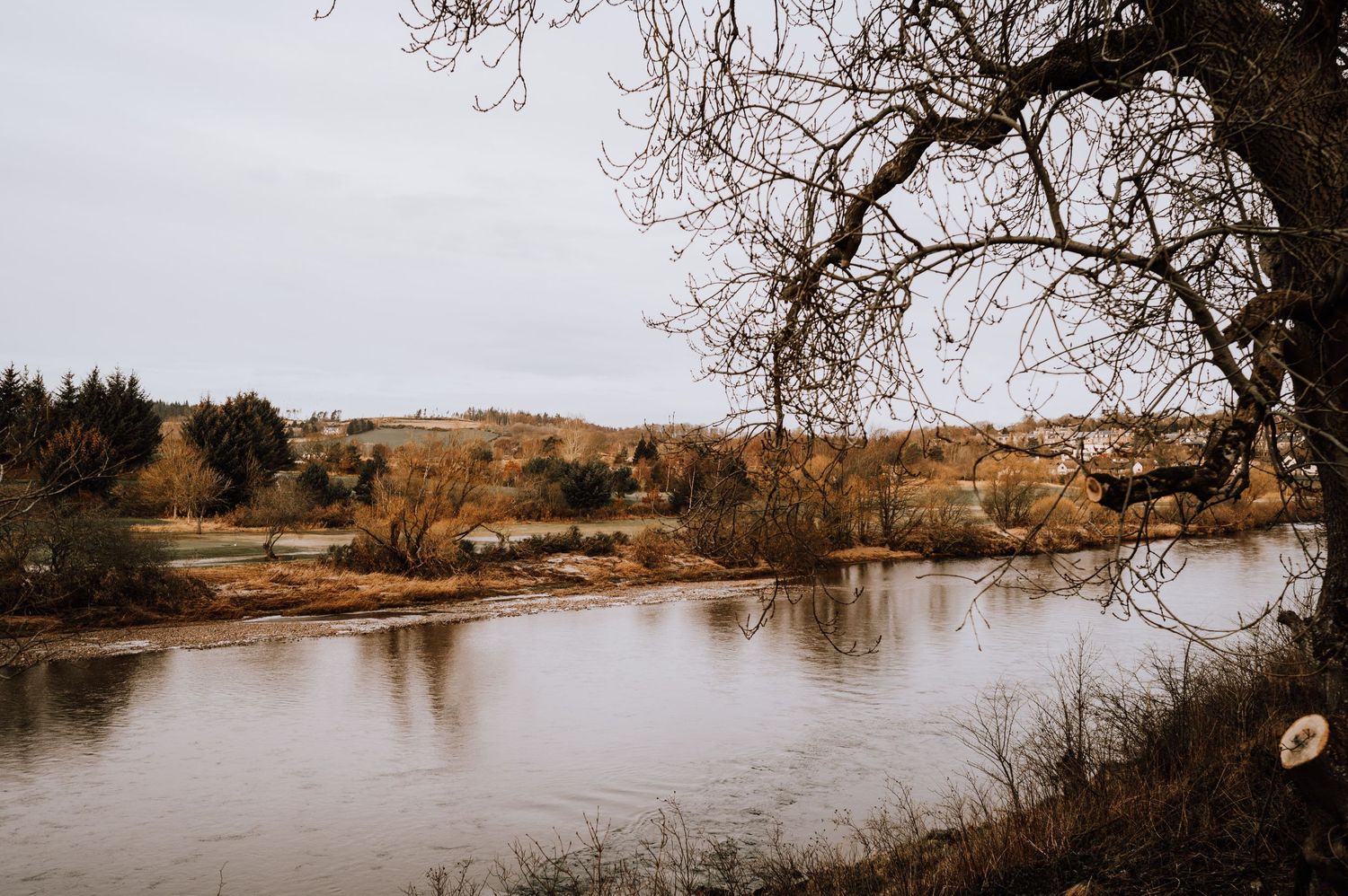 Serene autumn landscape with a still river reflecting trees and rolling hills.