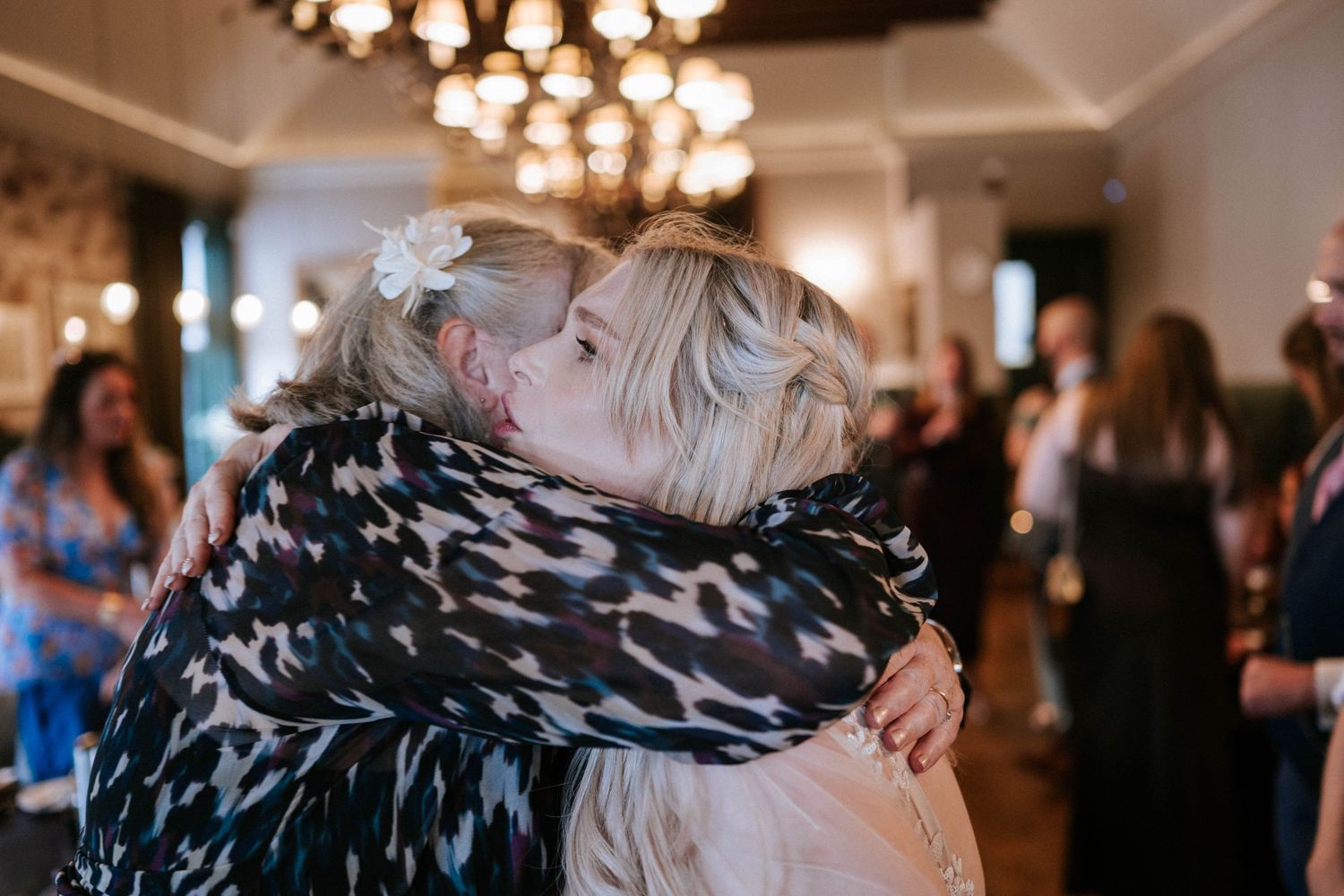 An emotional embrace during a wedding reception under crystal chandelier lighting.