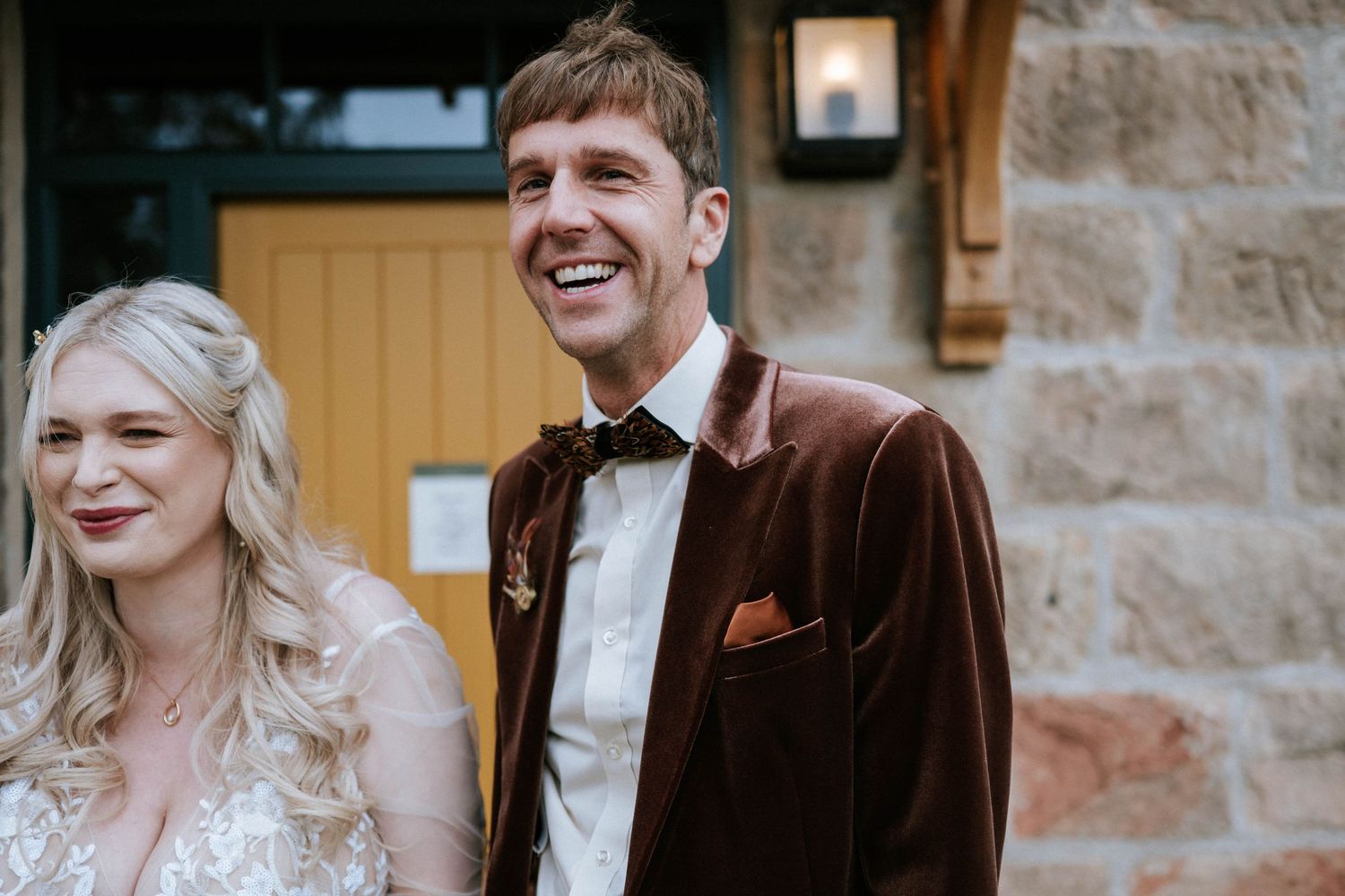 Wedding couple sharing joyful moments outside a stone building.