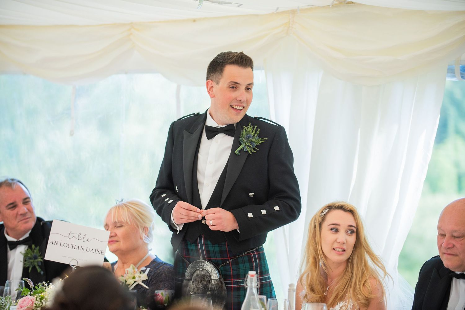 Wedding celebration in a white marquee tent with guests seated at decorated tables.