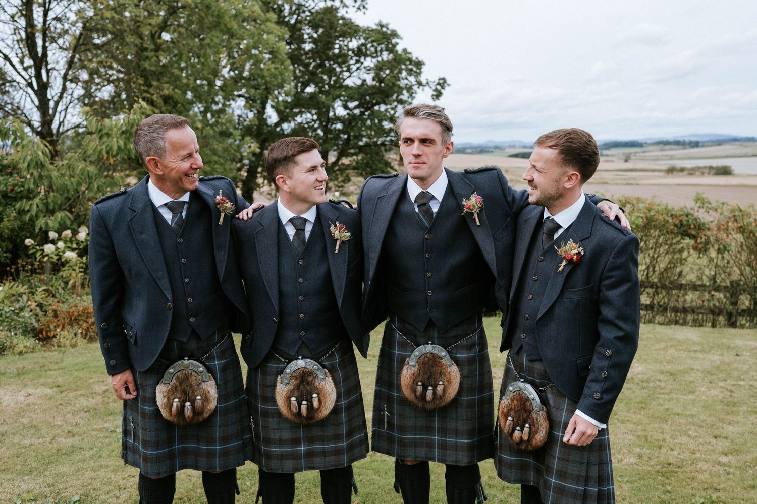 Groomsmen in traditional Scottish kilts standing together outdoors.