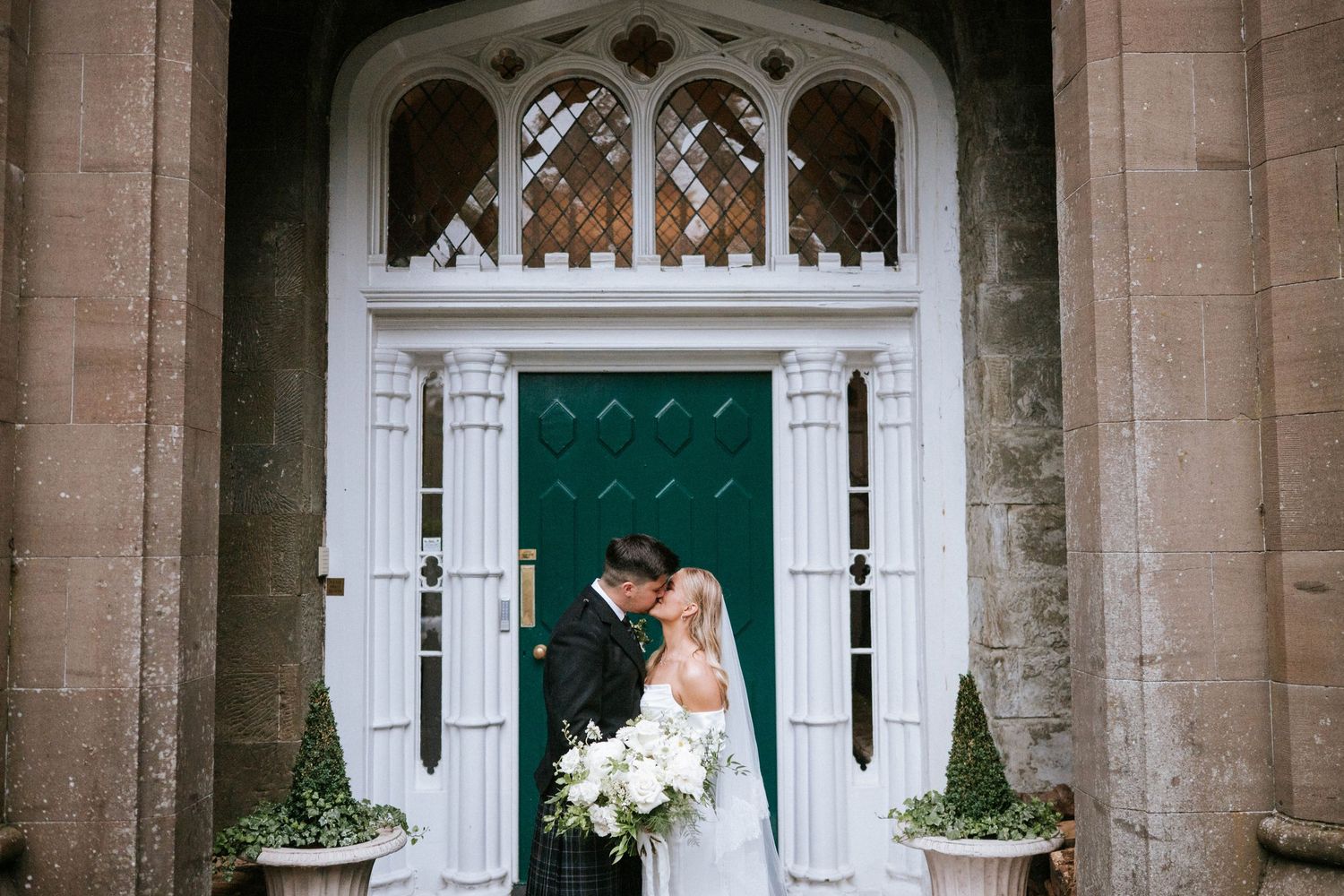 Romantic wedding couple poses in front of a grand green door with gothic architectural details.