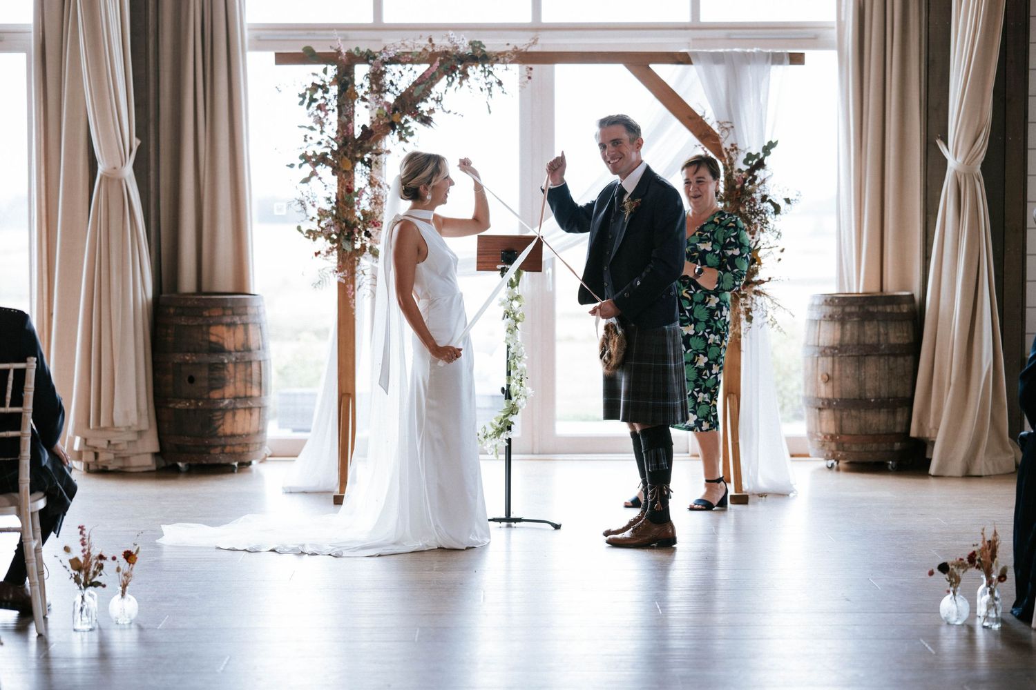 Wedding ceremony setup in an elegant indoor venue with white curtains and wooden barrels.