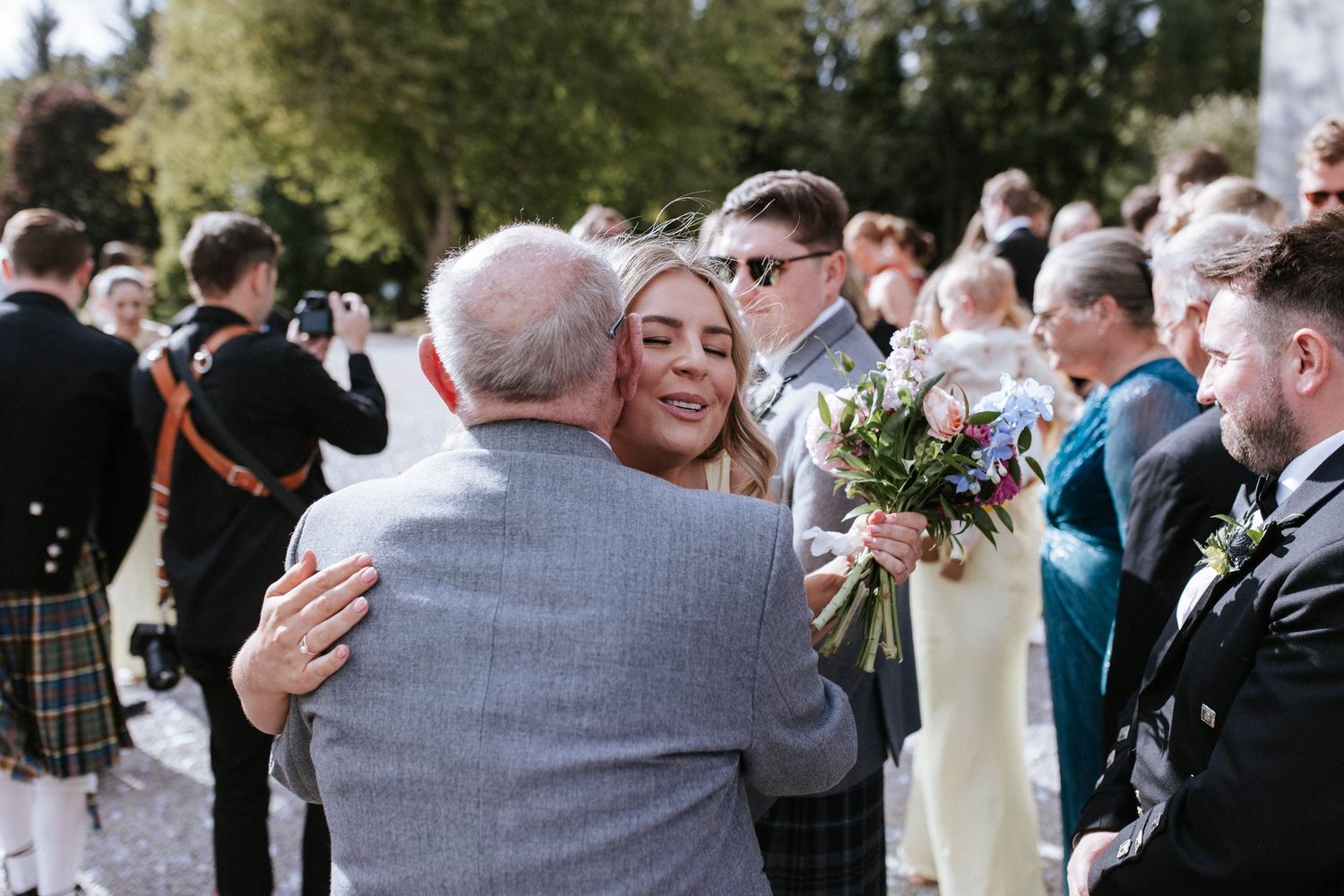 Emotional wedding reception moment with guests in kilts gathering outdoors.