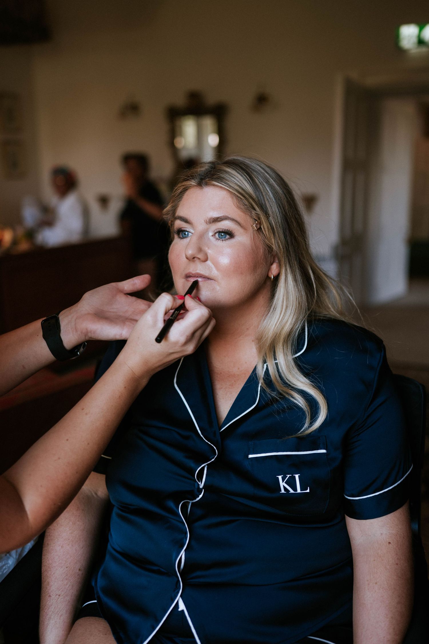 Wedding party member in navy robe having makeup applied during preparation.