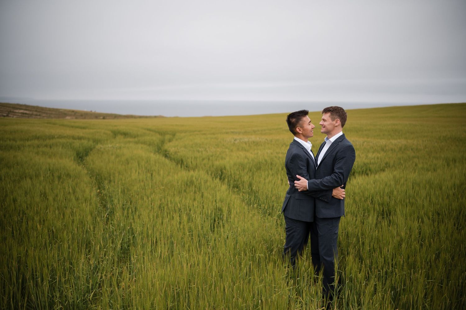 Same Sex Wedding Photography. Wedding party in formal black attire poses together in a golden wheat field at sunset.