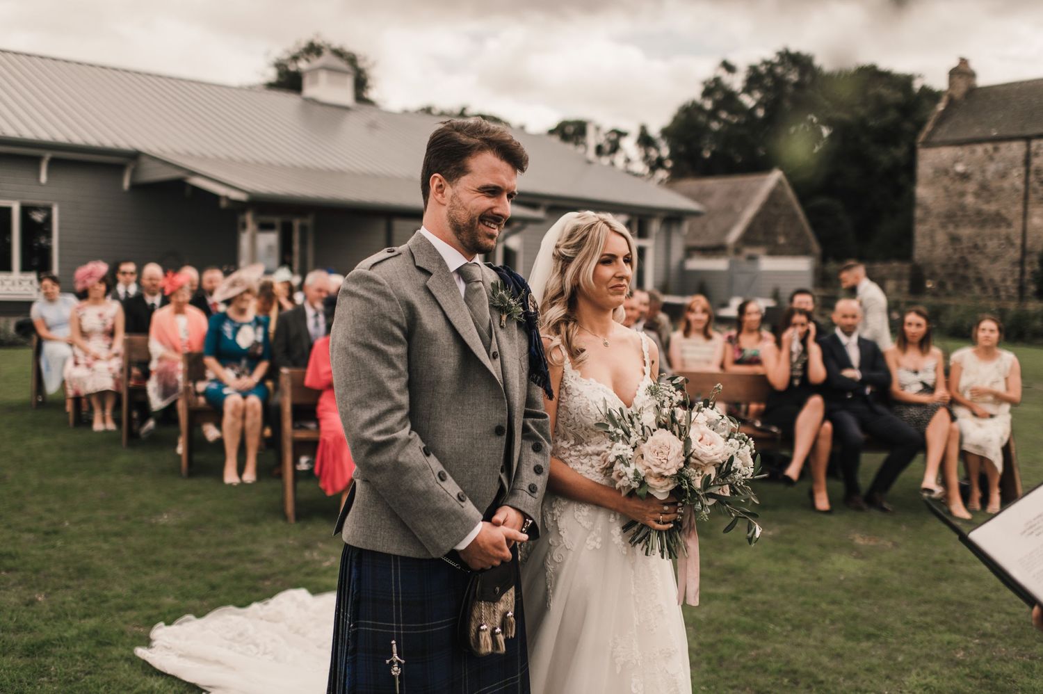 Newlyweds share joyful moment during outdoor ceremony with guests looking on.