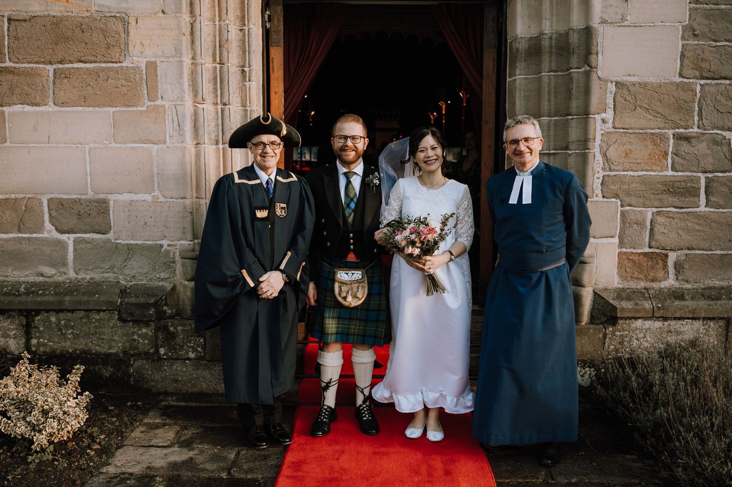 Wedding party poses on church steps with traditional Scottish kilts and formal attire.