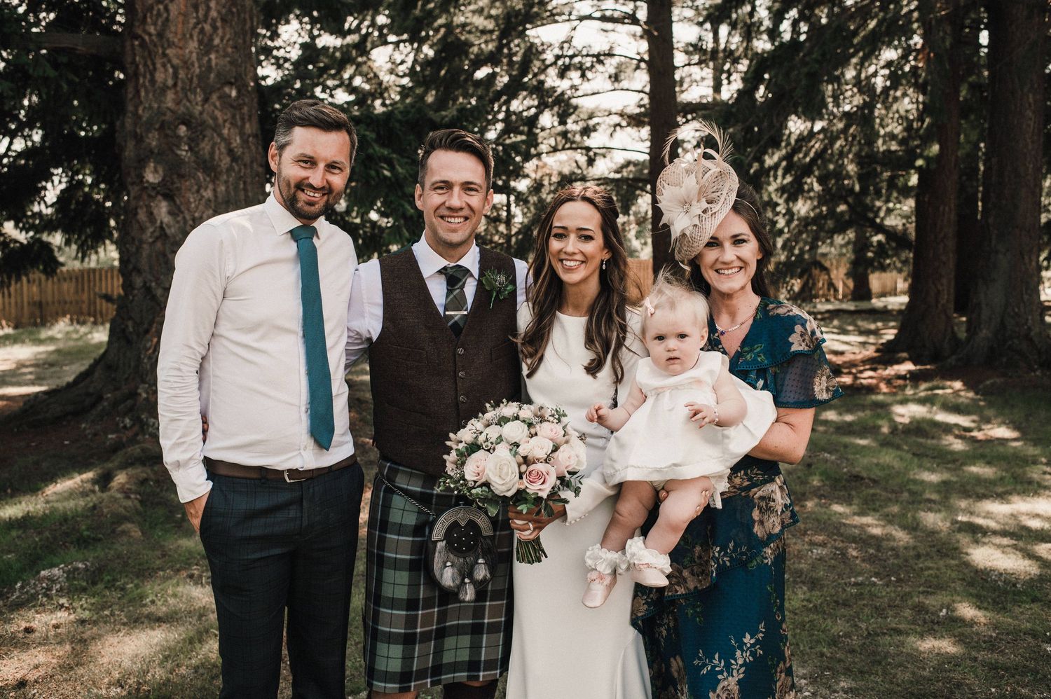 Wedding party in mix of formal wear and Scottish kilts poses in forest setting.