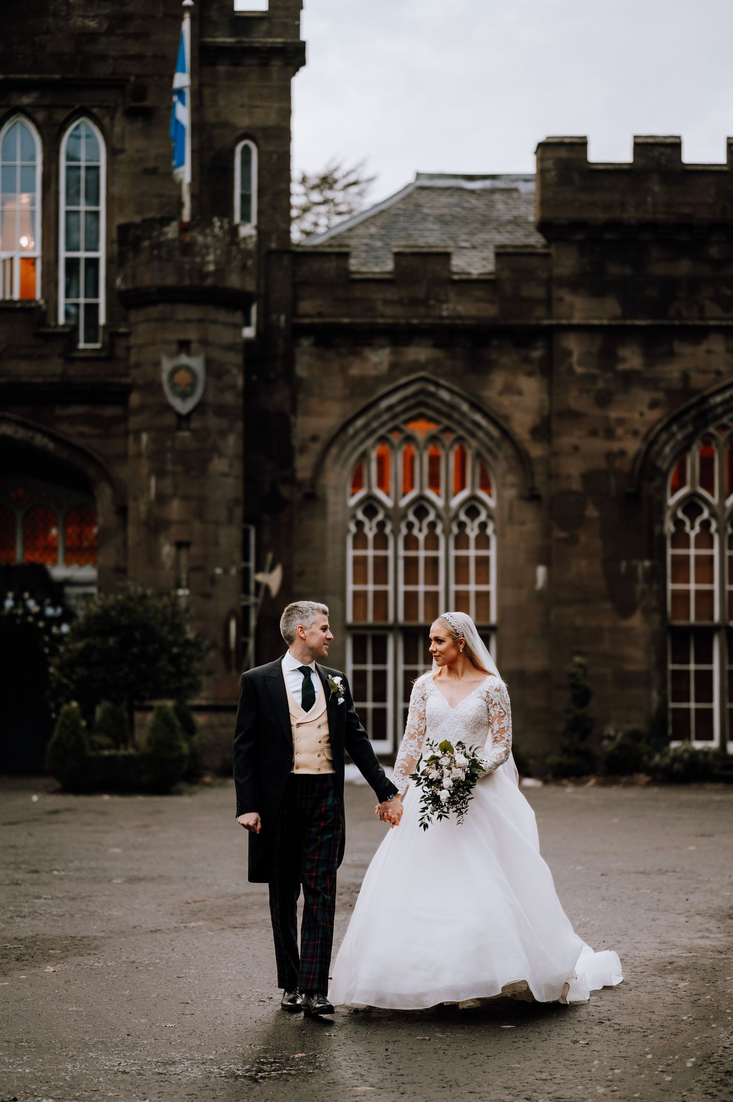A couple shares a sweet moment outside a gothic stone castle on their wedding day.