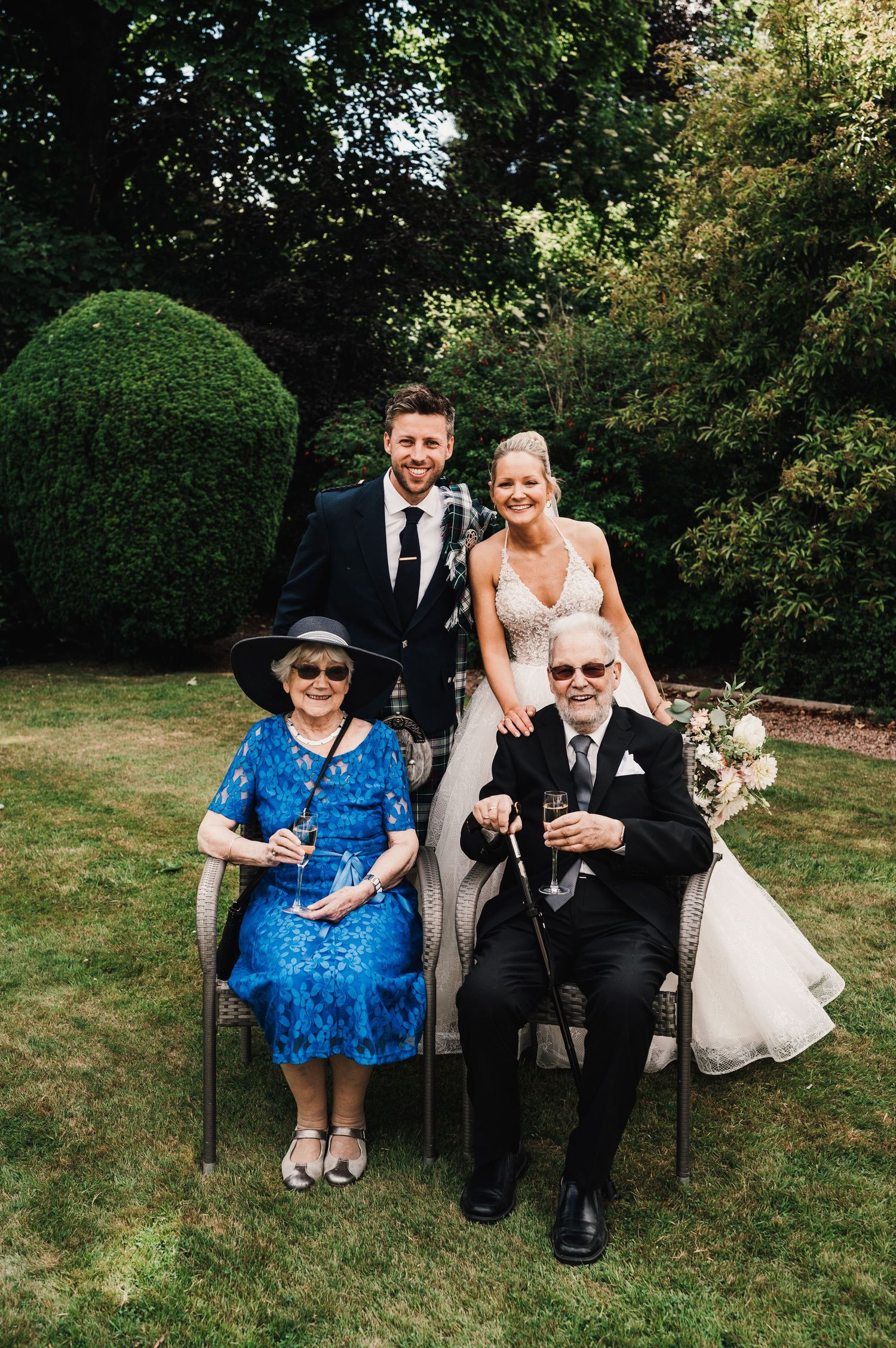Wedding portrait in a garden setting with family members seated in front.