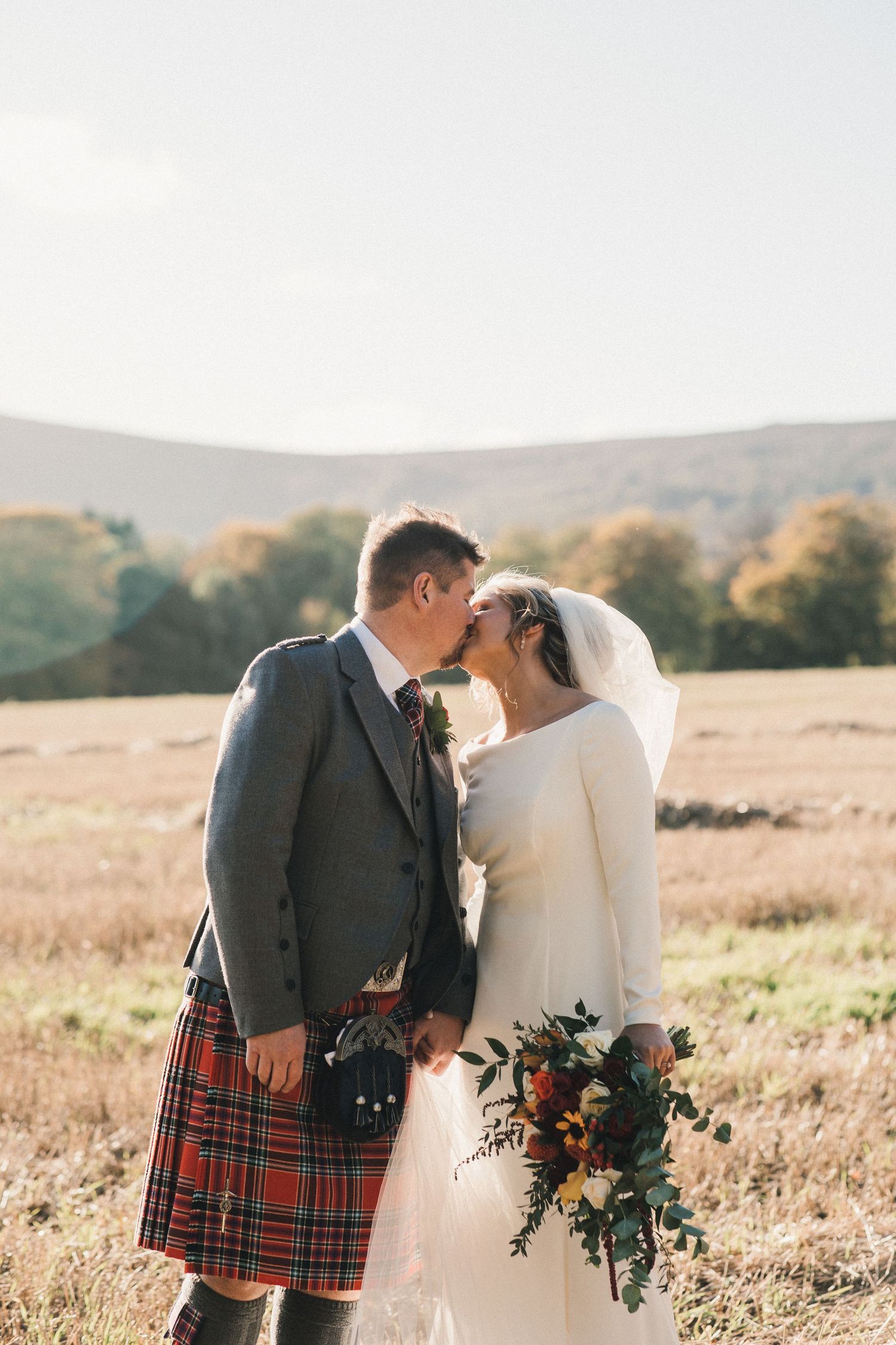 Traditional Scottish wedding portrait with groom in kilt and bride holding autumn bouquet.