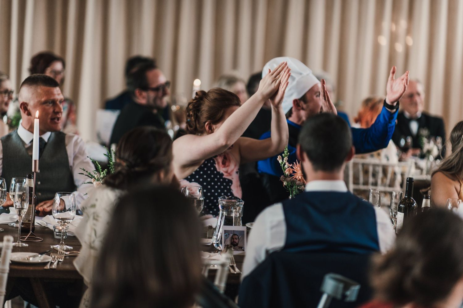 Wedding guests raise their hands in unison during a celebratory moment at the reception.