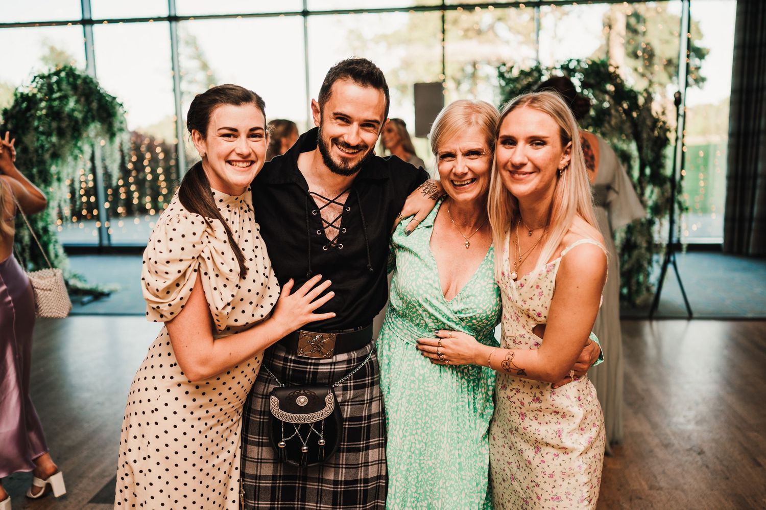 Wedding guests pose together with someone wearing a traditional Scottish kilt at the reception.