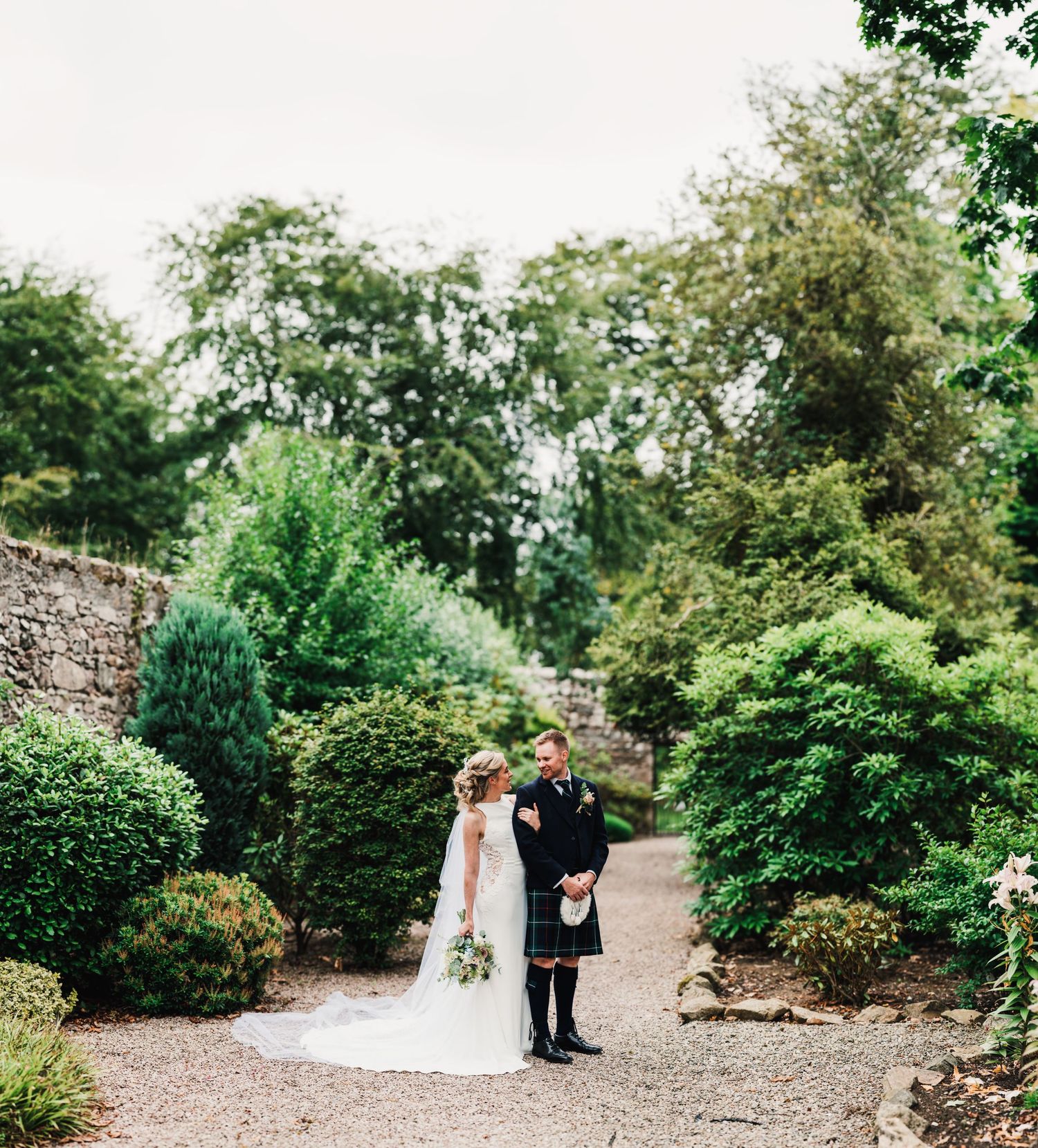 Couple walking along garden path surrounded by lush greenery at Scottish venue.