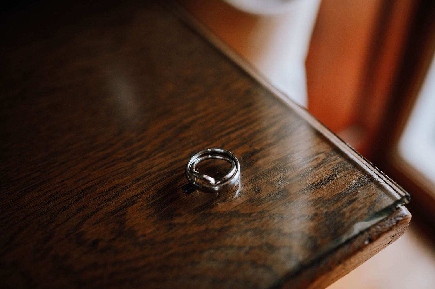 A wedding ring sits alone on a dark wooden surface in moody lighting.