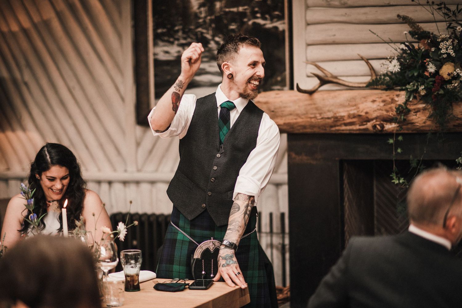 Speaker in formal attire gestures enthusiastically during a wedding reception speech.