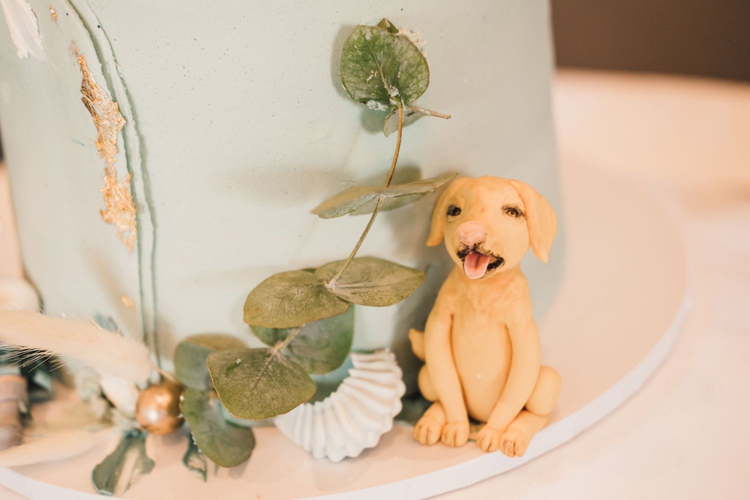 Small decorative clay dog figurine surrounded by eucalyptus leaves on white surface.