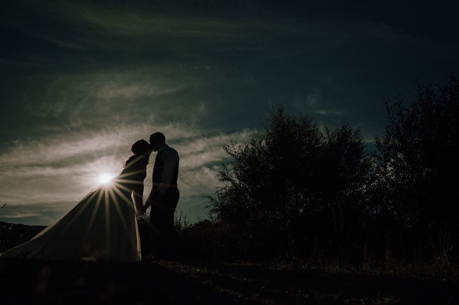 A romantic silhouette of newlyweds with sunburst at sunset.