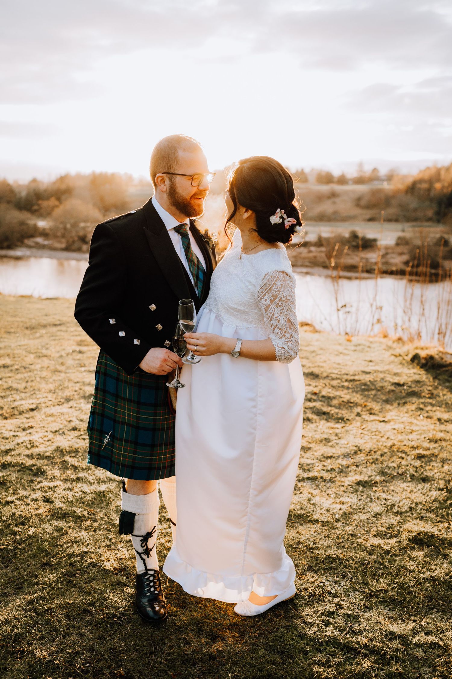 Golden hour wedding photo showing fusion of Scottish and Asian wedding traditions by a lake.