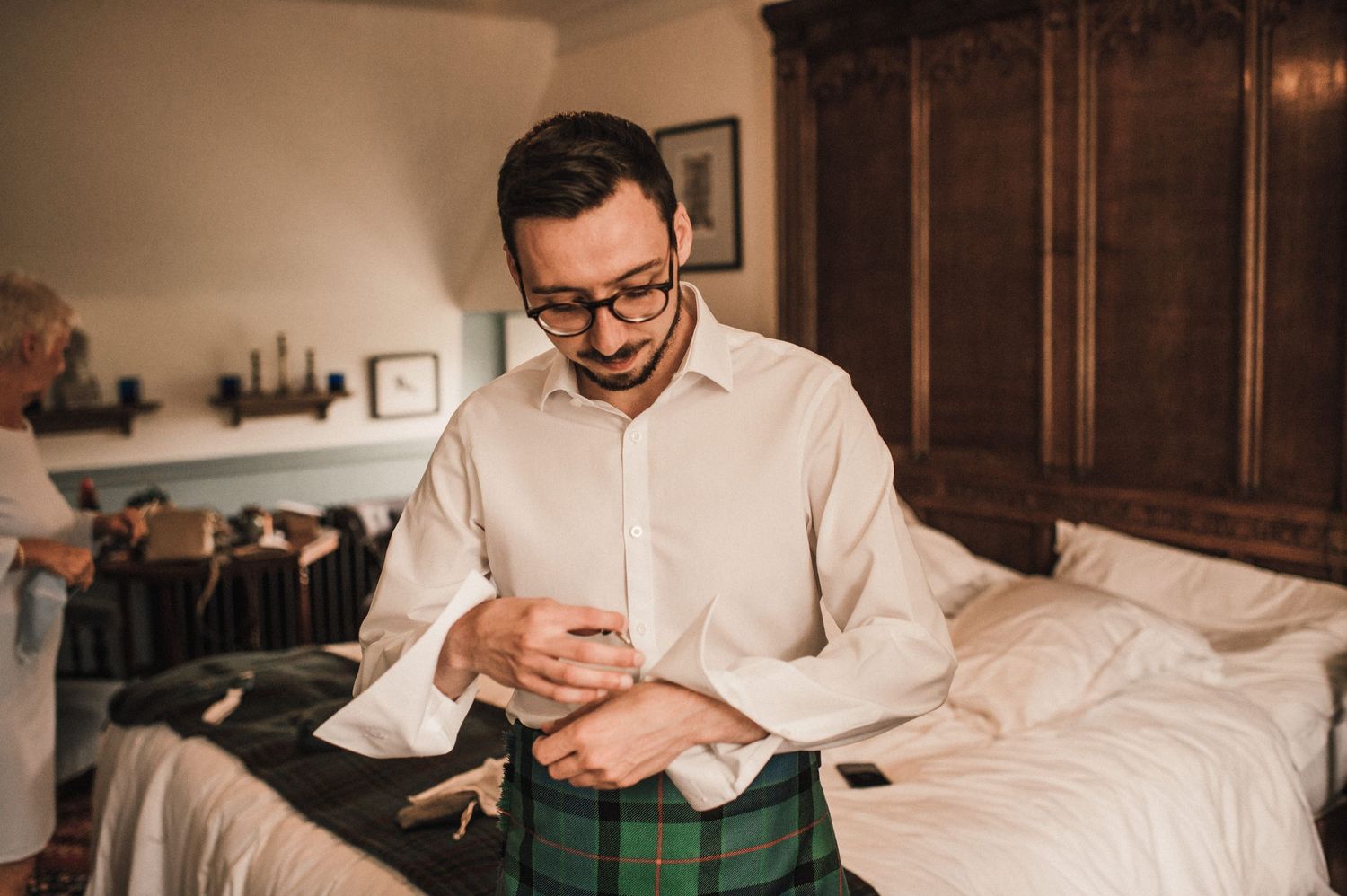 Someone adjusting cuffs while wearing a white dress shirt and traditional Scottish kilt.
