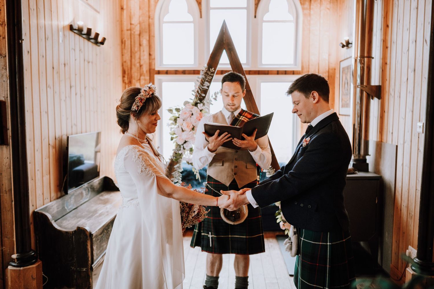 A wedding ceremony under a wooden arch with traditional Scottish elements and floral decorations.