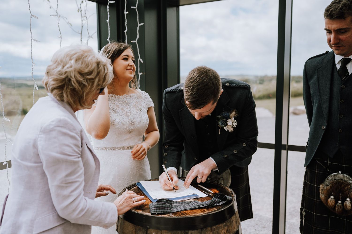 Wedding party gathers around a wooden barrel to sign the marriage certificate.