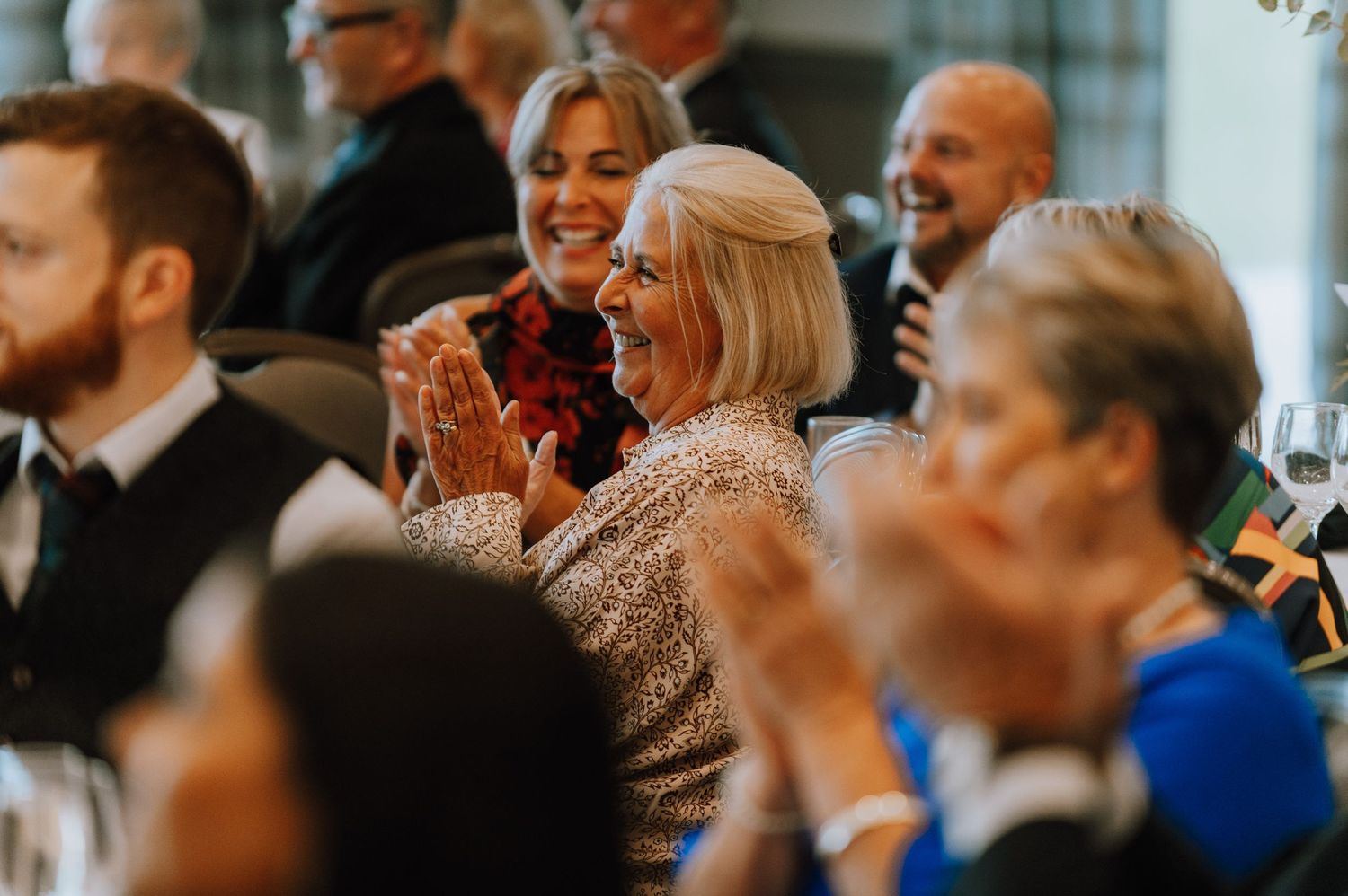 Wedding guests react with joy and laughter during reception speeches.