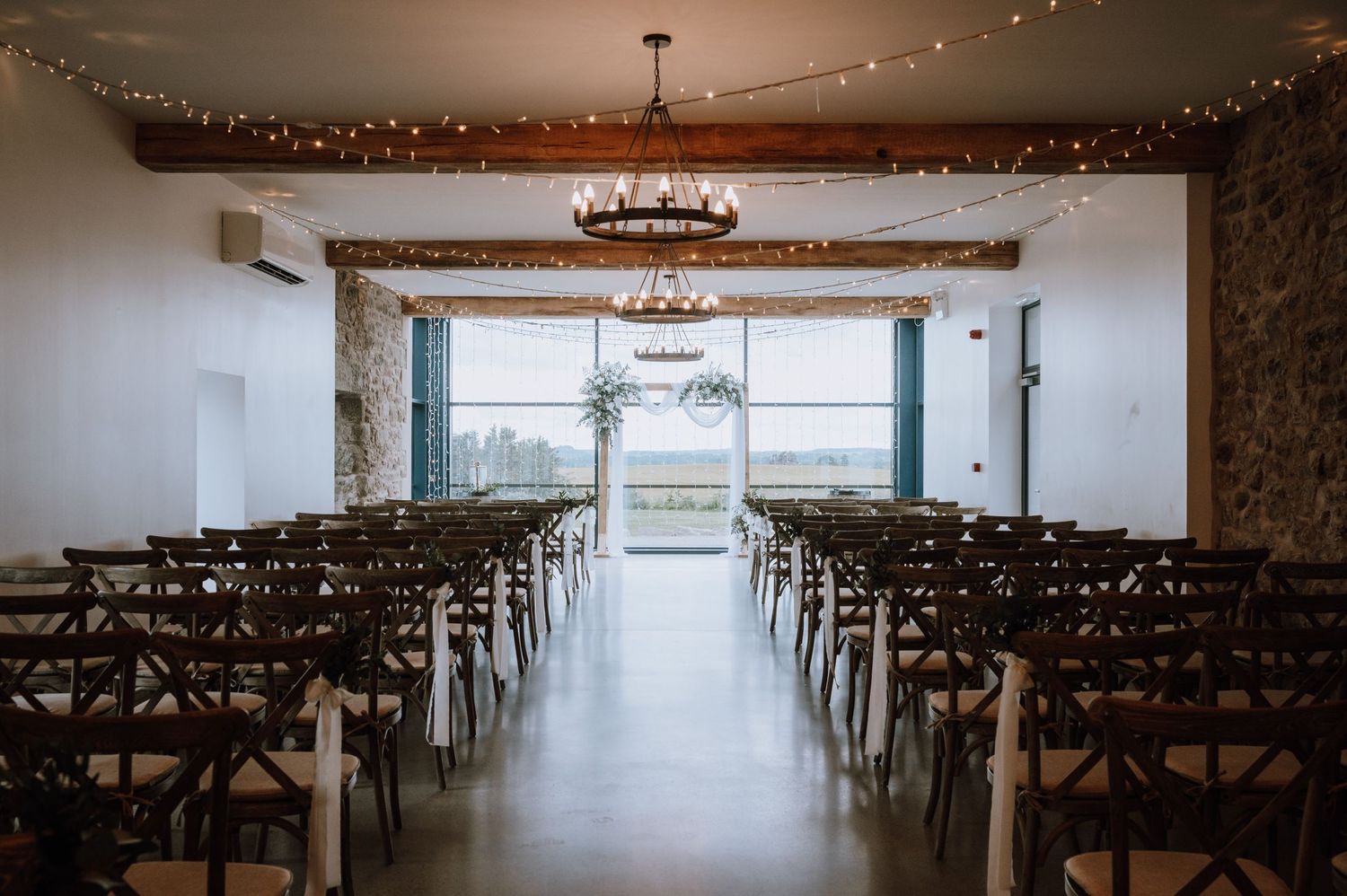 Wedding ceremony space with wooden chairs and string lights in an industrial modern venue.