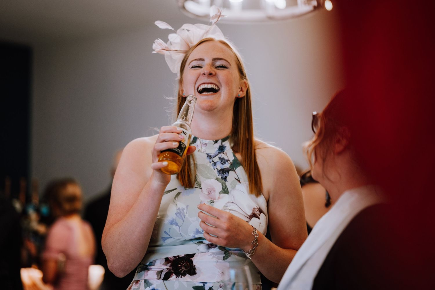 Wedding guest enjoying a drink and laughing during reception celebrations.