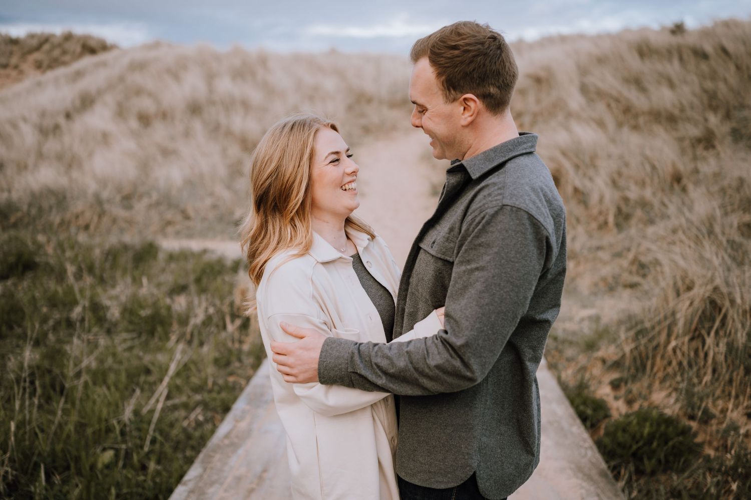 A couple embraces lovingly on a grassy hillside during an intimate outdoor photoshoot at sunset.